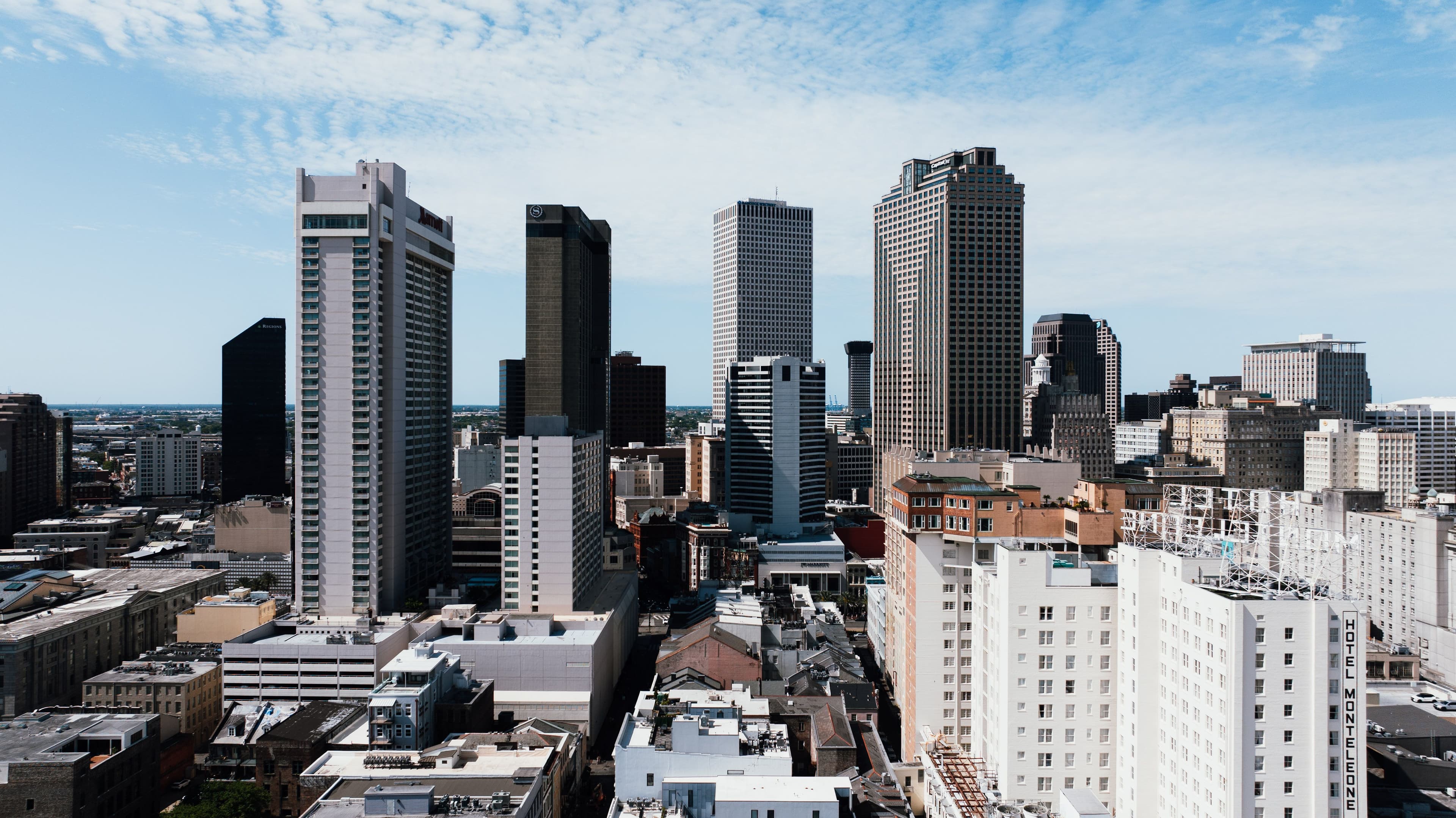 New Orleans skyline featuring tall skyscrapers and historic hotels under a bright blue sky.